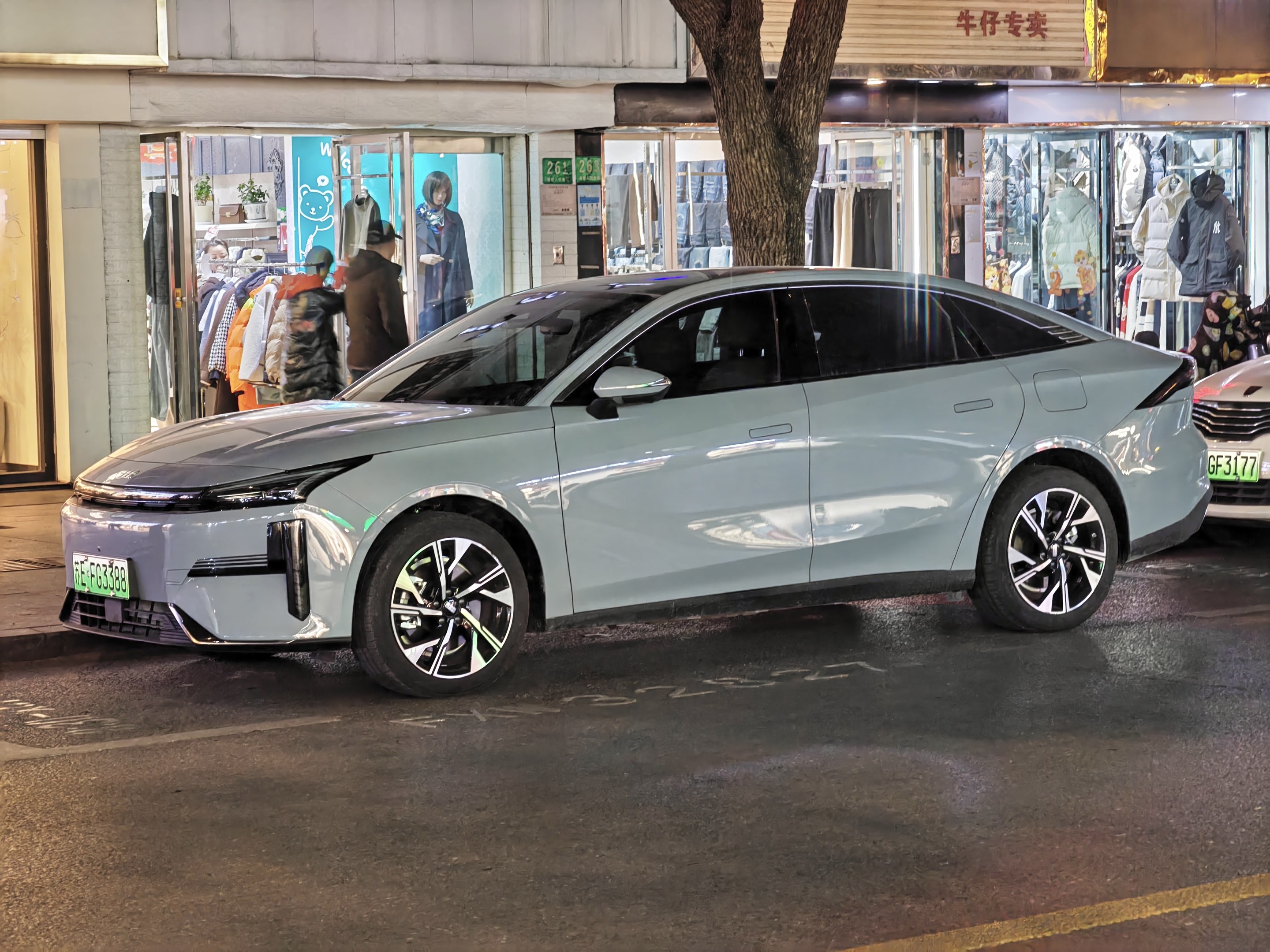 Elektrischer Mitsubishi Lancer EV auf einer nächtlichen Stadtstraße geparkt, umgeben von beleuchteten Schaufenstern und Schaufensterpuppen.