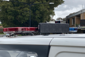 Ein Polizeiwagen mit eingeschaltetem Blaulicht steht am Straßenrand, umgeben von Gebäuden, Bäumen, Pfählen und Schildern mit Text, unter einem bewölkten Himmel, wahrscheinlich nach einer tödlichen Schießerei an einer Schule in Brisbane.