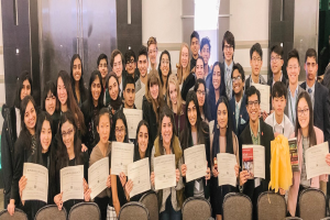 Gruppe von Menschen mit Urkunden, die auf Stühlen sitzen und vor einer Wand posieren, wahrscheinlich bei einer Abschlussfeier für das akademische Jahr 2019-2020.