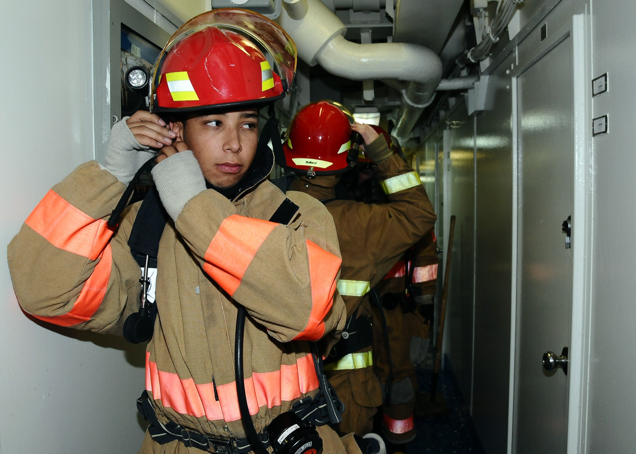 Feuerwehrleute in Uniform stehen in einem Raum mit Rohren und Geräten, wahrscheinlich während einer Übung.