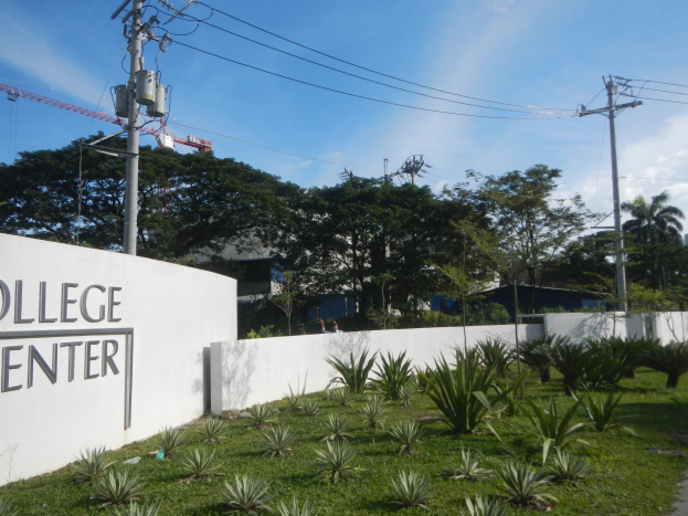 Eingang zu einem College-Center mit einem "College Center"-Schild an der Wand, umgeben von Grün, einem Weg, Strommasten, Bäumen, Gebäuden und einem bewölkten Himmel.