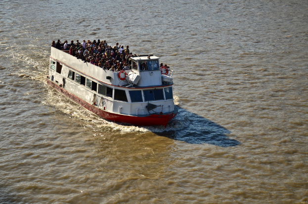 Ein Schiff, das auf dem Wasser segelt und voller Menschen auf dem Deck ist.