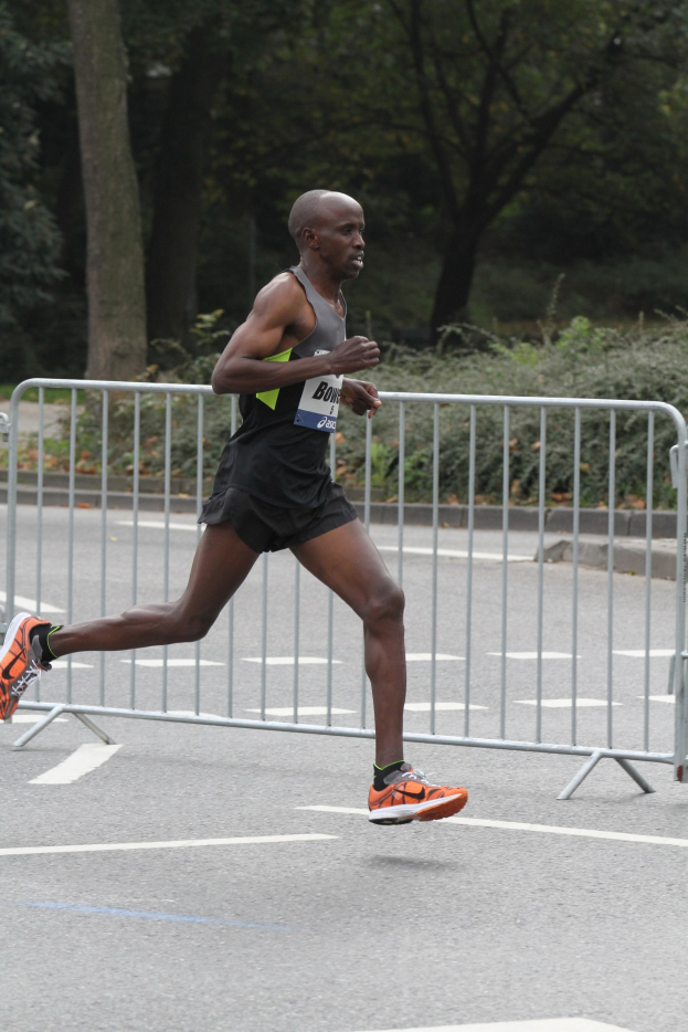 Ein Mann beim Laufen eines Marathons auf einer von B├Ąumen ges├Ąumten Stra├če, der sportliche Schuhe tr├Ągt.