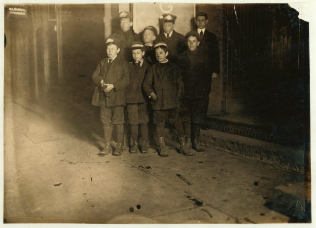 Eine Gruppe junger Jungs steht nebeneinander auf einem Gehweg vor einem Geb├Ąude, Schwarz-Wei├č-Foto.