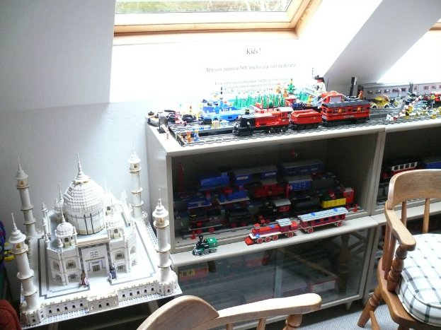Ein Glasfenster oben in der Mitte, ein Stuhl rechts, eine Vitrine mit SpielzeughÃ¤usern in einer Reihe und ein Spielzeug-Taj Mahal links auf einem Schreibtisch.