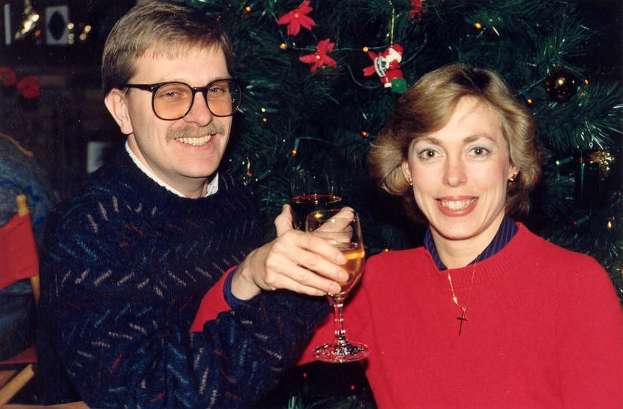 Ein Paar lächelt, während es Gläser mit Wein hält, mit einem Weihnachtsbaum im Hintergrund.