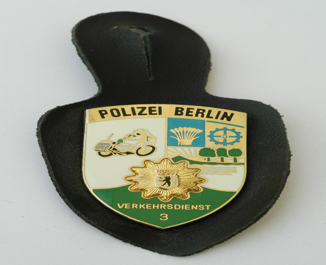 Ein schildförmiges Polizewemzeichen mit der Aufschrift "Polizei Berlin" auf einem blauen Hintergrund, einem weißen Rand und einem zentralen weißen Stern, das auf einer Oberfläche liegt.