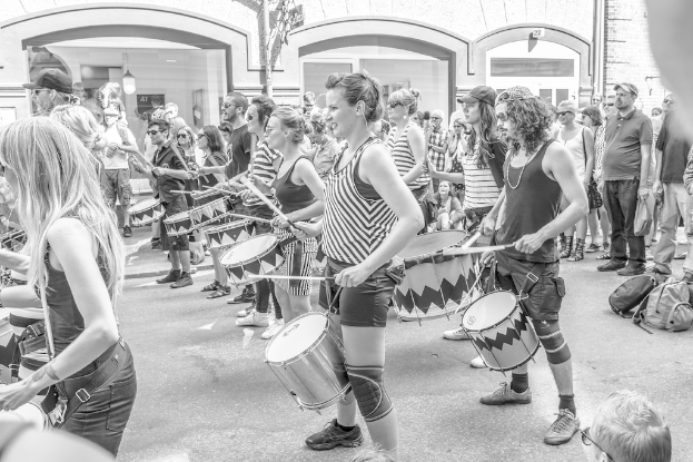 Eine Gruppe von Menschen, die draußen Musikinstrumente spielen, mit einer geschlossenen Glastür und einer Lampe im Hintergrund.
