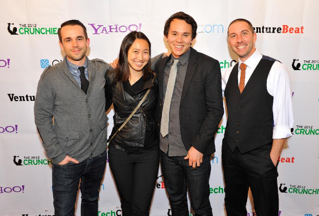 Eine Gruppe strahlender Menschen, die vor der Kamera posen, mit einem Sponsorenbanner im Hintergrund.