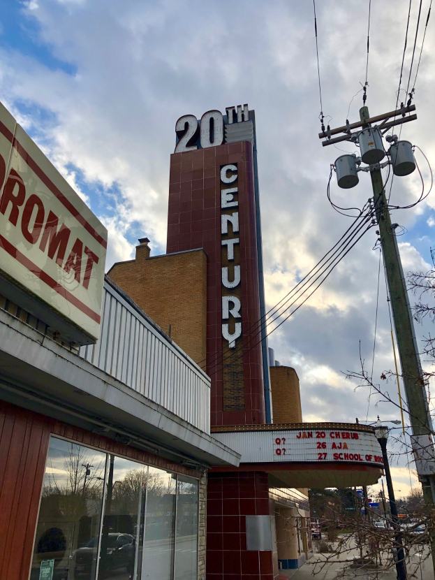 Außenansicht des 20th Century Theatre in Detroit, Michigan, mit Glaswänden, Namensschildern, umgeben von Bäumen und Strommasten mit Drähten unter einem bewölkten Himmel.