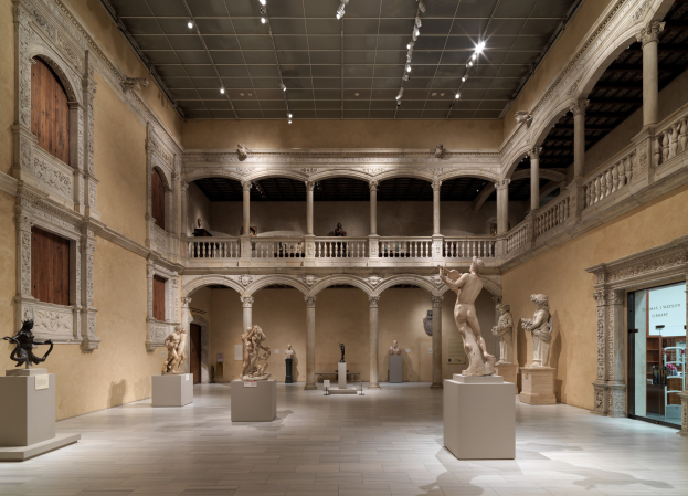 Große Museumsgalerie mit zahlreichen Statuen und Skulpturen auf Sockeln, architektonischen Elementen einschließlich Wänden, Säulen, Geländern und einer beleuchteten Decke, mit einigen Besuchern.