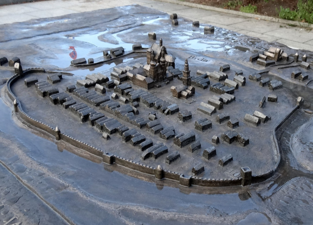 Eine Modellstadt in einer Pfütze umgeben von Gebäuden, Bäumen, Pflanzen und einer Hintergrundwand.