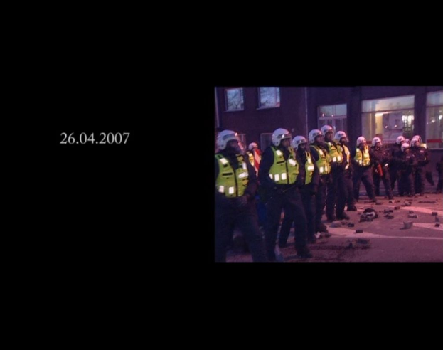 Gruppe von Polizisten in Helmen und Jacken vor einem Gebäude mit Fenstern, mit einem Datum auf der linken Seite.