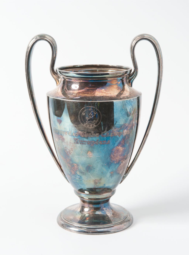 Der UEFA Champions League-Pokal, ein stählerner Becher mit zwei Griffen und einem blauen und silbernen Farbschema, mit der Inschrift "UEFA Champions League", vor einem weißen Hintergrund dargestellt.