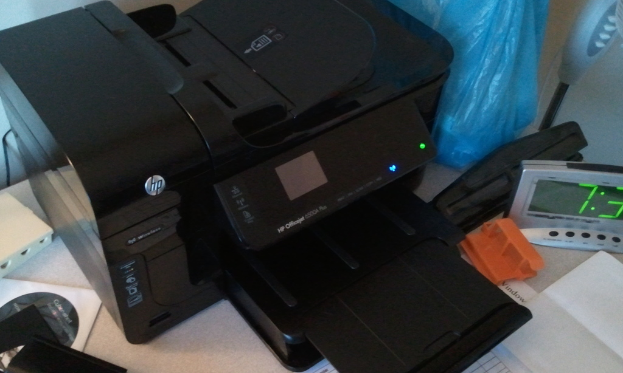 Ein digitaler Timer, ein HP-Drucker, eine blaue Polythenhülle, eine CD in ihrer Hülle, Papier und einige andere Gegenstände sind auf einem Tisch angeordnet.