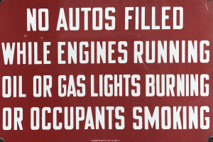 Ein rotes Schild mit weißer Schrift, das vor dem Betanken von Fahrzeugen warnt, wenn der Motor läuft, Öl- oder Gaslichter brennen oder Insassen rauchen.