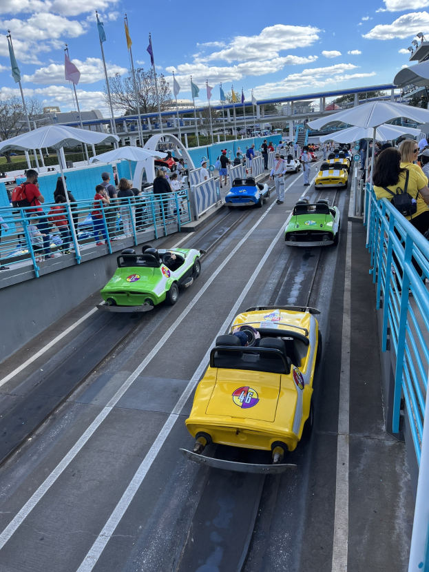 Gruppe von Menschen, die eine Achterbahn an Disney's Hollywood Studios fahren, umgeben von Geländern und Fahnen, mit Bäumen und Gebäuden im Hintergrund unter einem bewölkten Himmel.