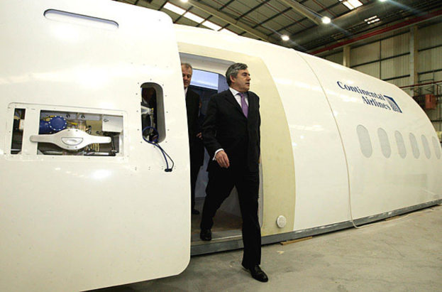 Ein Flugzeugprototyp mit der Aufschrift "Continental Airlines", mit zwei Personen daneben, vor einer Wand, Lampen und einigen anderen Gegenständen.