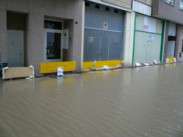 Flutstraße mit Wasser bis zur Höhe von Fenstern und Türen, überschwemmte Umgebung und nahe Objekte.