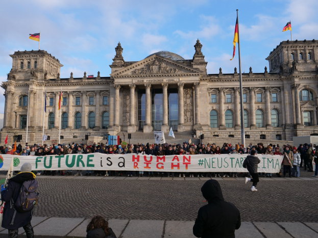 Eine Gruppe von Menschen steht vor dem Reichstaggebäude in Berlin und hält ein Banner mit der Aufschrift "Zukunft ist ein Human Neustar ima" und ist von Flaggen umgeben.