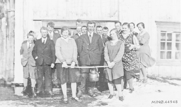 Schwarzes und weißes Foto von Menschen, die lächeln und ein Band halten, vor einem Gebäude mit einem Fenster und einer Tür, bei der Einweihung einer neuen Schule.