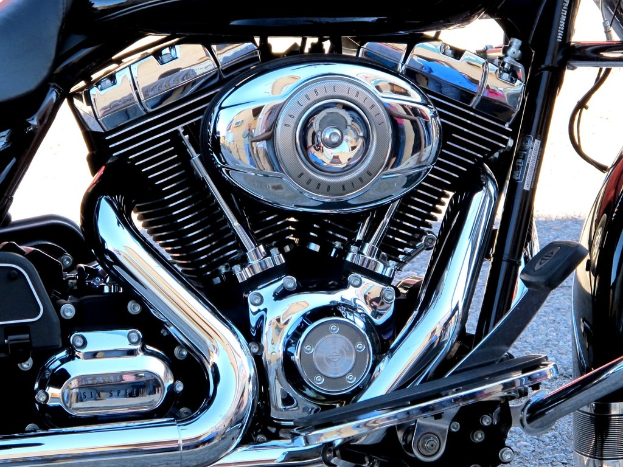 Eine Sammlung von Motorradteilen, einschließlich eines Motors, eines Kühlers, eines Auspuffrohrs, von Zahnrädern, Stangen, Muttern und Drähten.