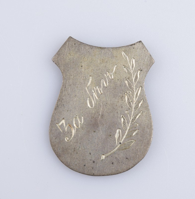 Silbernes Abzeichen mit einem Lorbeerkranz und der Inschrift "50-jähriges Jubiläum" auf einem weißen Hintergrund.