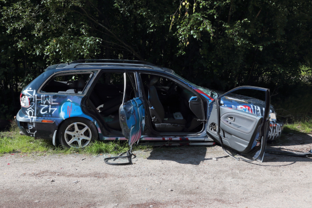 Ein beschädigtwagen am Straßenrand mit Gras und Bäumen im Hintergrund.