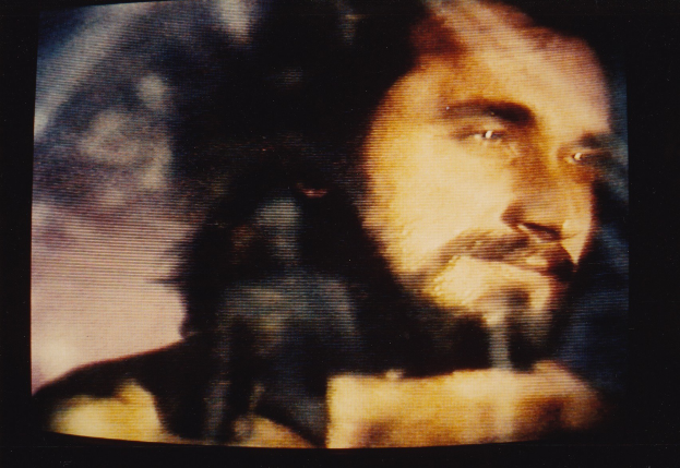 Zwei maskierte und handschuhgetragene Chirurgen führen eine Gesichtsoperation an einer Frau durch, die auf einem Bett liegt, mit einem Fenster und Bäumen im Hintergrund.