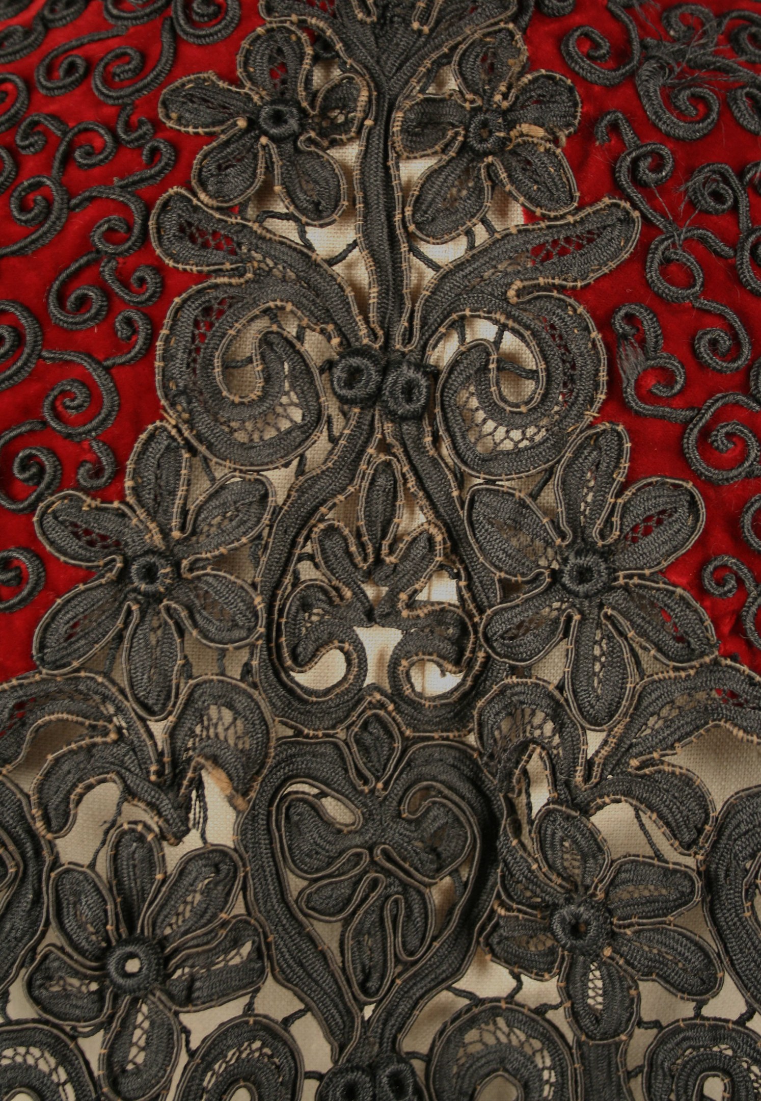 Nahaufnahme eines roten Kleides mit schwarzer Spitze, das detaillierte Spitzenmuster auf dem roten Stoff zeigt.