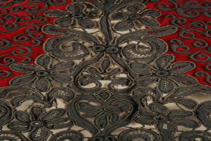 Nahaufnahme eines roten Kleides mit schwarzer Spitze, das detaillierte Spitzenmuster auf dem roten Stoff zeigt.