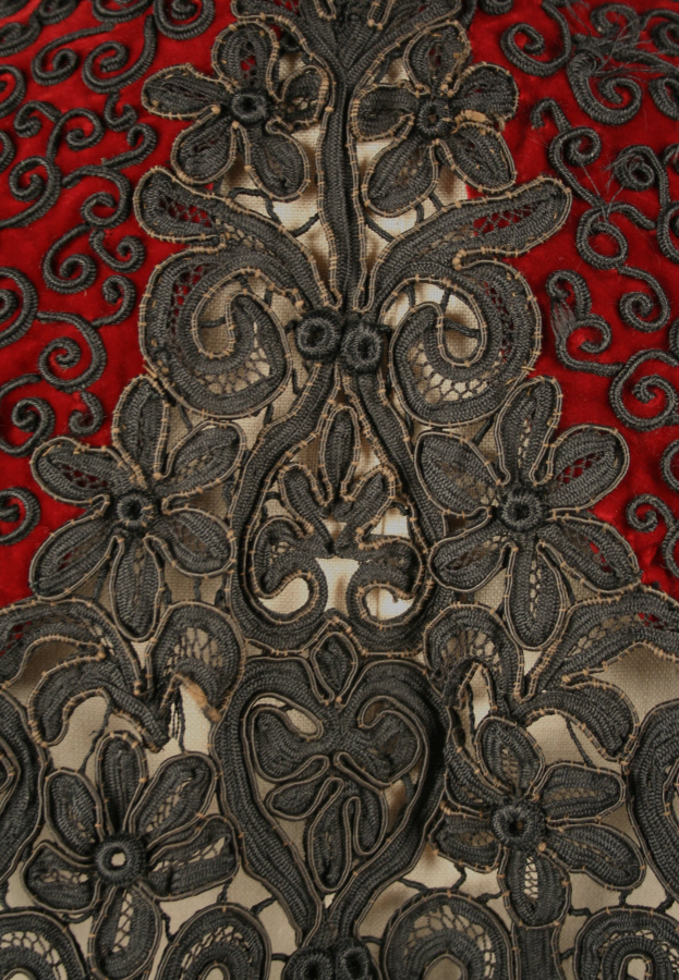 Nahaufnahme eines roten Kleides mit schwarzer Spitze, das detaillierte Spitzenmuster auf dem roten Stoff zeigt.