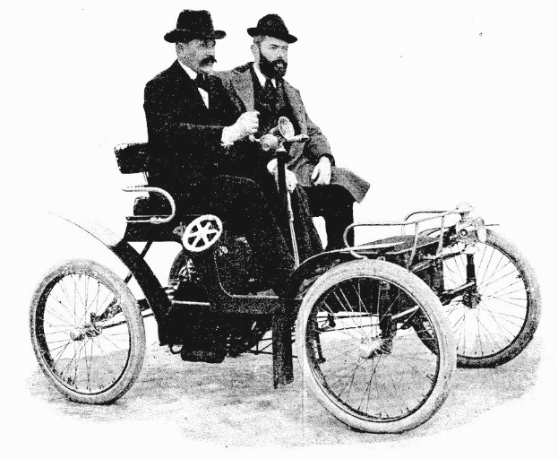 Zwei Männer in Blazern und Hüten sitzen in einem vintage-Schwarz-Weiß-Auto.