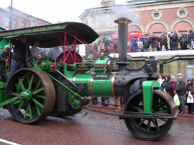 Ein Motor ist zentral positioniert mit Gebäuden oben und Menschen auf der rechten Seite des Bildes.