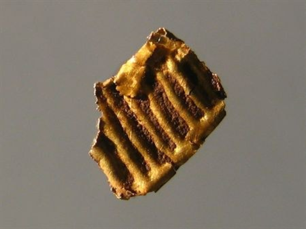 Ein kleines, unregelmäßig geformtes Goldstück auf einem soliden grauen Hintergrund.