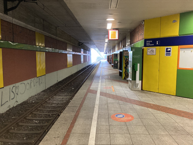 Ein Bahnsteig in Berlin Hauptbahnhof, Deutschland, mit einem stehenden Zug auf den Schienen, von der Decke beleuchtet, Graffiti an einer linken Wand und ein paar Gegenständen auf der rechten Seite.