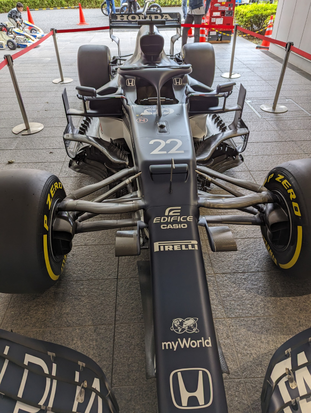 Ein McLaren Mercedes MP4-23 Formel-1-Auto, das beim Singapur Grand Prix ausgestellt wird, umgeben von Barrieren, Verkehrskegeln, Menschen, Fahrzeugen, Pflanzen, Bäumen und einem Gebäude im Hintergrund.