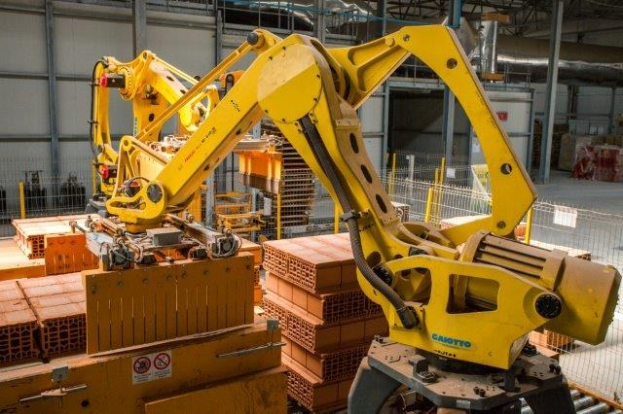 Großes industrielles Lagerhaus mit gestapelten Kisten, Überkopfkranen, Zaun, Pfählen und einer fernen Wand in einer Fertigungsumgebung.