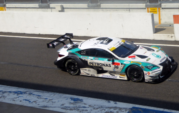 Mercedes-AMG GT3 Rennauto auf einer Rennstrecke mit Text auf dem Fahrzeug und einer Glaswand im Hintergrund.