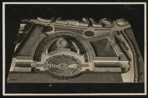 Schwarzes und weißes Rahmenfoto eines detaillierten Modellkonzertsaals mit einer zentralen Kuppel, Steinwänden, Metalldach und einer hell beleuchteten Bühne, umgeben von einer Menge.