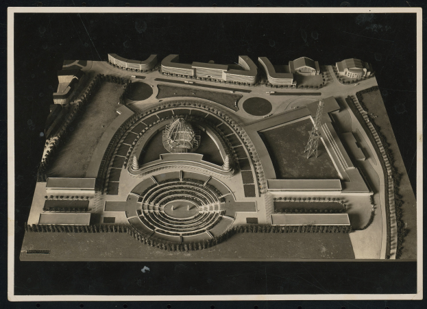 Schwarzes und weißes Rahmenfoto eines detaillierten Modellkonzertsaals mit einer zentralen Kuppel, Steinwänden, Metalldach und einer hell beleuchteten Bühne, umgeben von einer Menge.