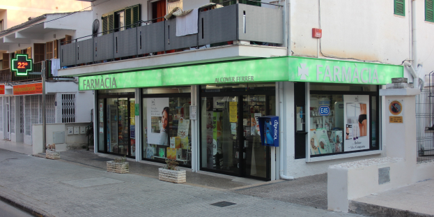 Apotheke an einer Straßenecke mit Gebäuden, Fahrzeugen und einem klaren Himmel im Hintergrund.