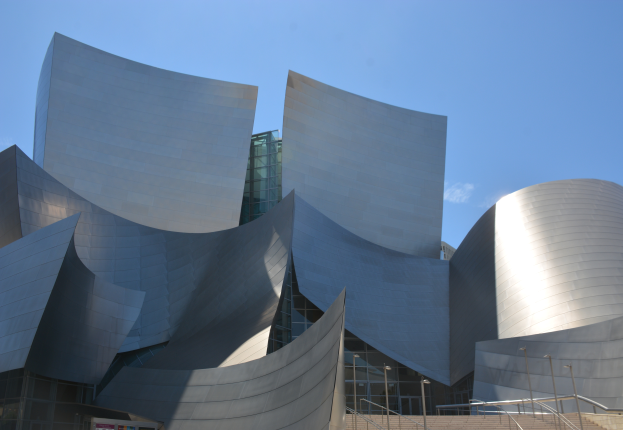 Das Künstler-Konzertgebäude in Los Angeles, ein modernes Gebäude mit Glaswänden, Treppen mit Geländern, die zum Eingang führen, umgeben von Laternenmasten, mit einer Tafel mit Text im Vordergrund und einem bewölkten Himmel im Hintergrund.