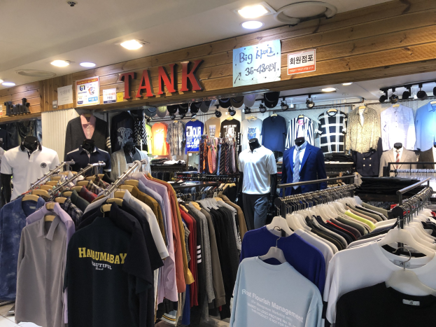 Kleidungsgeschäft mit zahlreichen T-Shirts auf Display, Schaufensterpuppen, die die neuesten Modellen präsentieren, Texttafeln an den Wänden und moderner Deckenbeleuchtung.