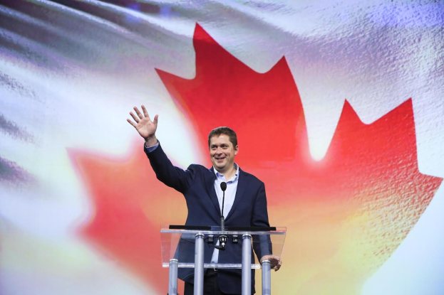 Der kanadische Premierminister Alex Salmond steht an einem Podium mit Mikrofonen, lächelt vor einer kanadischen Flagge, wobei ein Bildschirm im Hintergrund zu sehen ist.