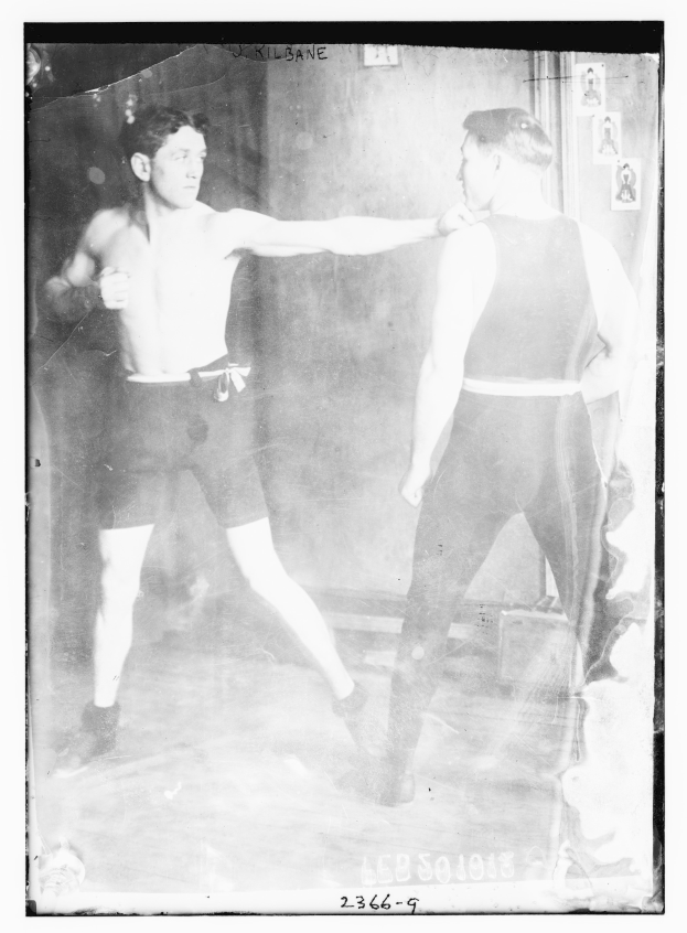 Schwarzes und weißes Foto von zwei Boxern im Ring mit Postern an der Hintergrundwand und Text unten.