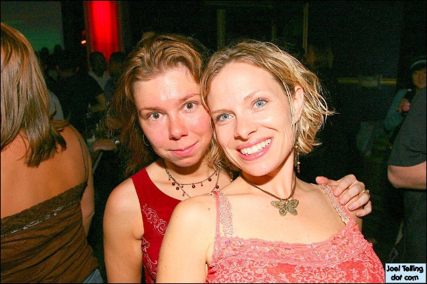 Eine Gruppe von Menschen mit zwei lächelnden Frauen in der Mitte und einem Licht im Hintergrund.