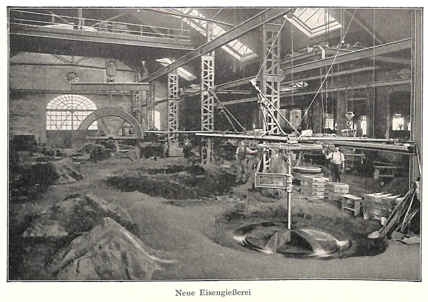 Schwarzes und weißes Foto einer Fabrikhalle mit Arbeitern, die Maschinen bedienen, umgeben von Metallstangen und -pfählen, beschriftet mit 'Neue Eisenglebeerei, die erste Fabrik in Deutschland' unten.