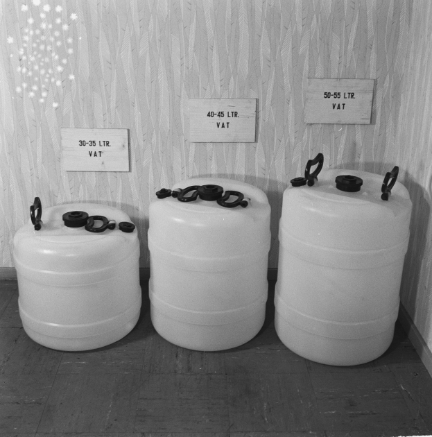 Drei weiße Plastikkanister in Dreiecksform auf einem Holzboden, mit einer Wand im Hintergrund.