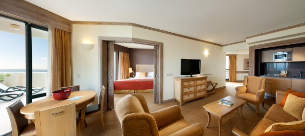 Ein Wohnzimmer mit einem Fernseher, einer Couch, Stühlen, Kissen, einer Mikrowelle, einem Bett und einem Tisch.